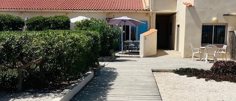 A wooden pathway leading to a building with a red-tiled roof and a covered outdoor seating area.