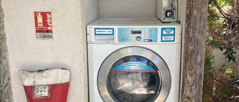 A compact laundry facility with a front-loading washing machine, a red bag labeled 'EXTINTEUR,' and a small control panel.