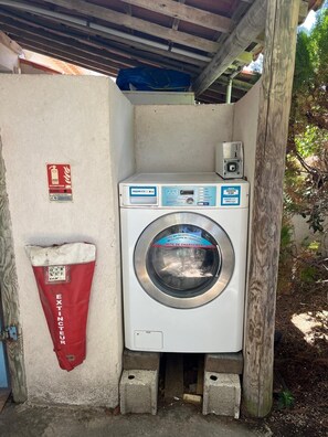 A compact laundry facility with a front-loading washing machine, a red bag labeled 'EXTINTEUR,' and a small control panel. - Giens Peninsula - ocean view - direct access to the beach - La Bergerie - La Capte (Hyères)