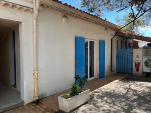 A building with a white exterior, blue doors, and a small garden area with a planter. - Giens Peninsula - ocean view - direct access to the beach - La Bergerie - La Capte (Hyères)