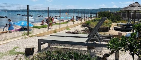 Zona de playa con área de natación cercada, sillas de descanso y una estructura de techo de paja.