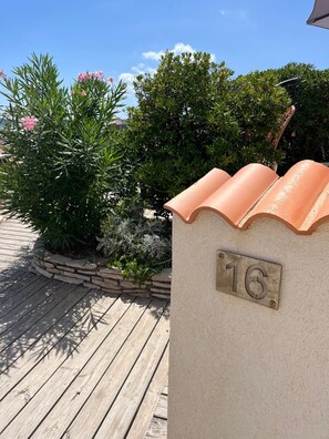 A house number plaque on a wall, a wooden deck, and a garden with various plants and flowers. - Giens Peninsula - ocean view - direct access to the beach - La Bergerie - La Capte (Hyères)