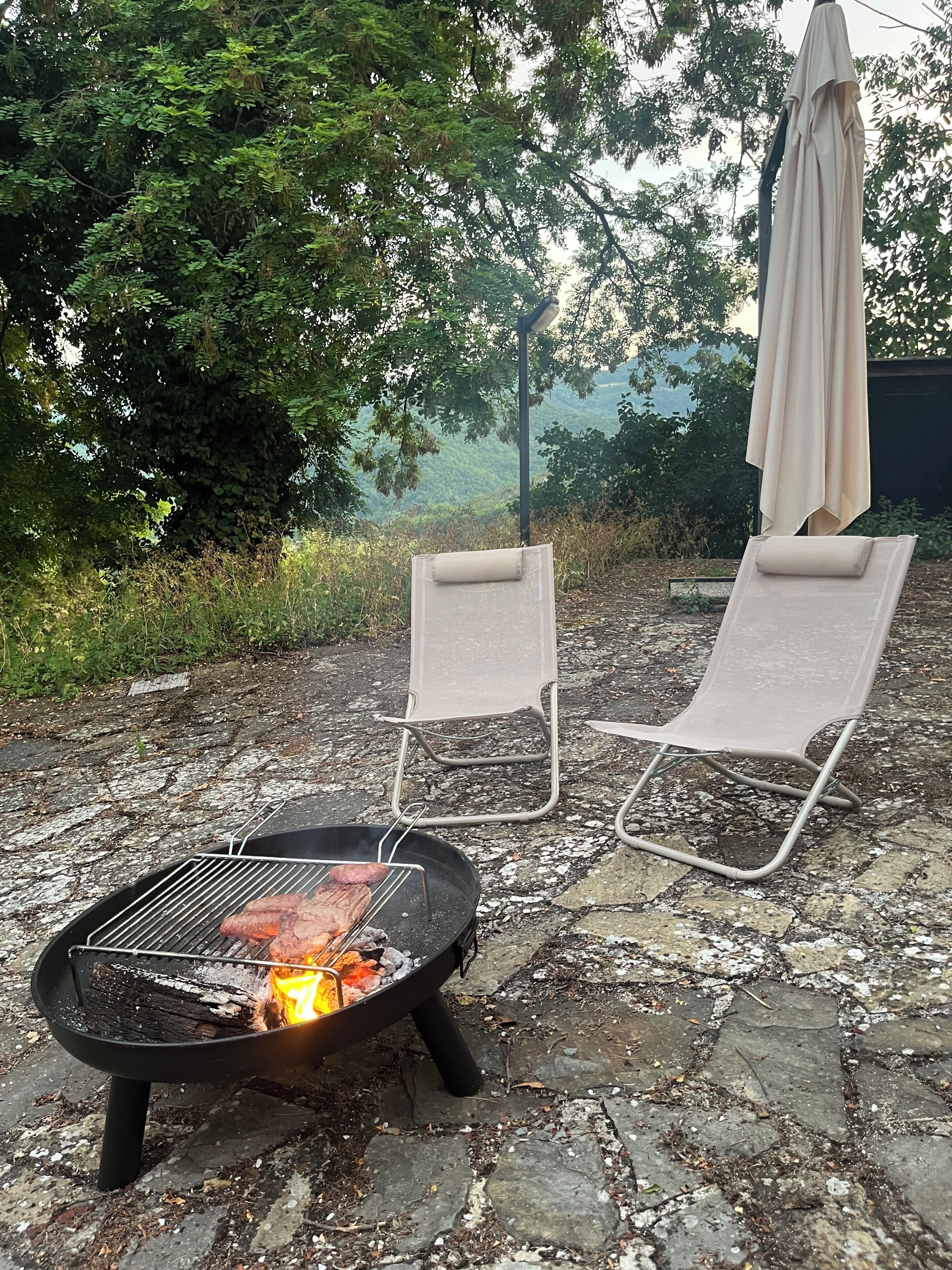 Una griglia con cibo, due poltrone da relax e un ombrellone in un giardino.