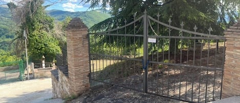 A gated entrance with stone walls and a metal gate, surrounded by trees and a mountainous backdrop.