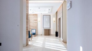 A modern hotel corridor with a wooden accent wall, a framed artwork, and a blue chair.