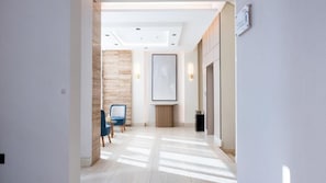 A modern hotel corridor with a wooden accent wall, a framed artwork, and a blue chair.