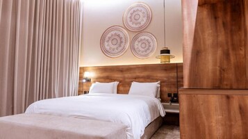 Una habitación de hotel con cama, cabecera de madera, mesita de noche con lámpara y un mueble grande de madera.