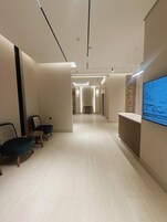 Un pasillo moderno de hotel con zonas de estar y una pantalla de televisión en la pared.