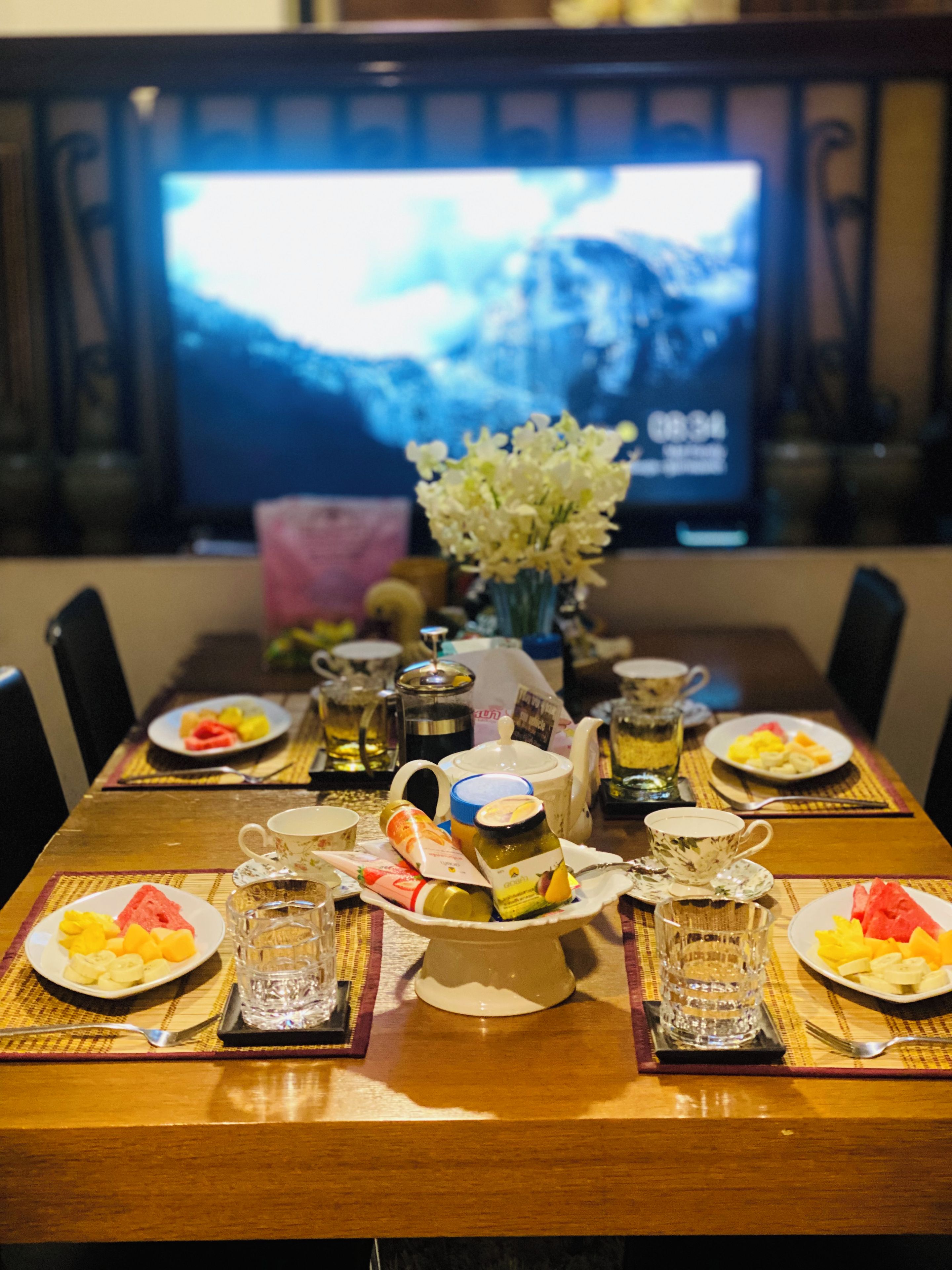 A dining table set with plates of fruit, a vase of flowers, and various condiments.