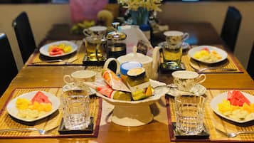 A dining table set with plates of fruit, a vase of flowers, and various condiments.