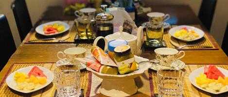 A dining table set with plates of fruit, a vase of flowers, and various condiments.