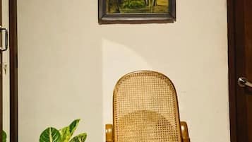 A room with a wicker chair, a potted plant, and a framed picture on the wall.