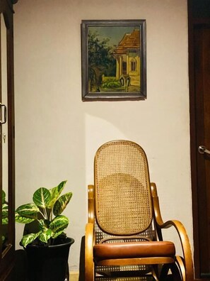 Una habitación con una silla de mimbre, una planta en maceta y un cuadro en la pared.