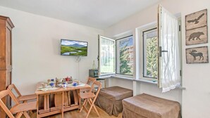 Una habitación con una mesa de comedor, sillas, un televisor y una ventana con cortinas.