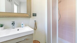 Un baño con lavamanos blanco, un espejo, ducha con azulejos rosados y una puerta de madera.