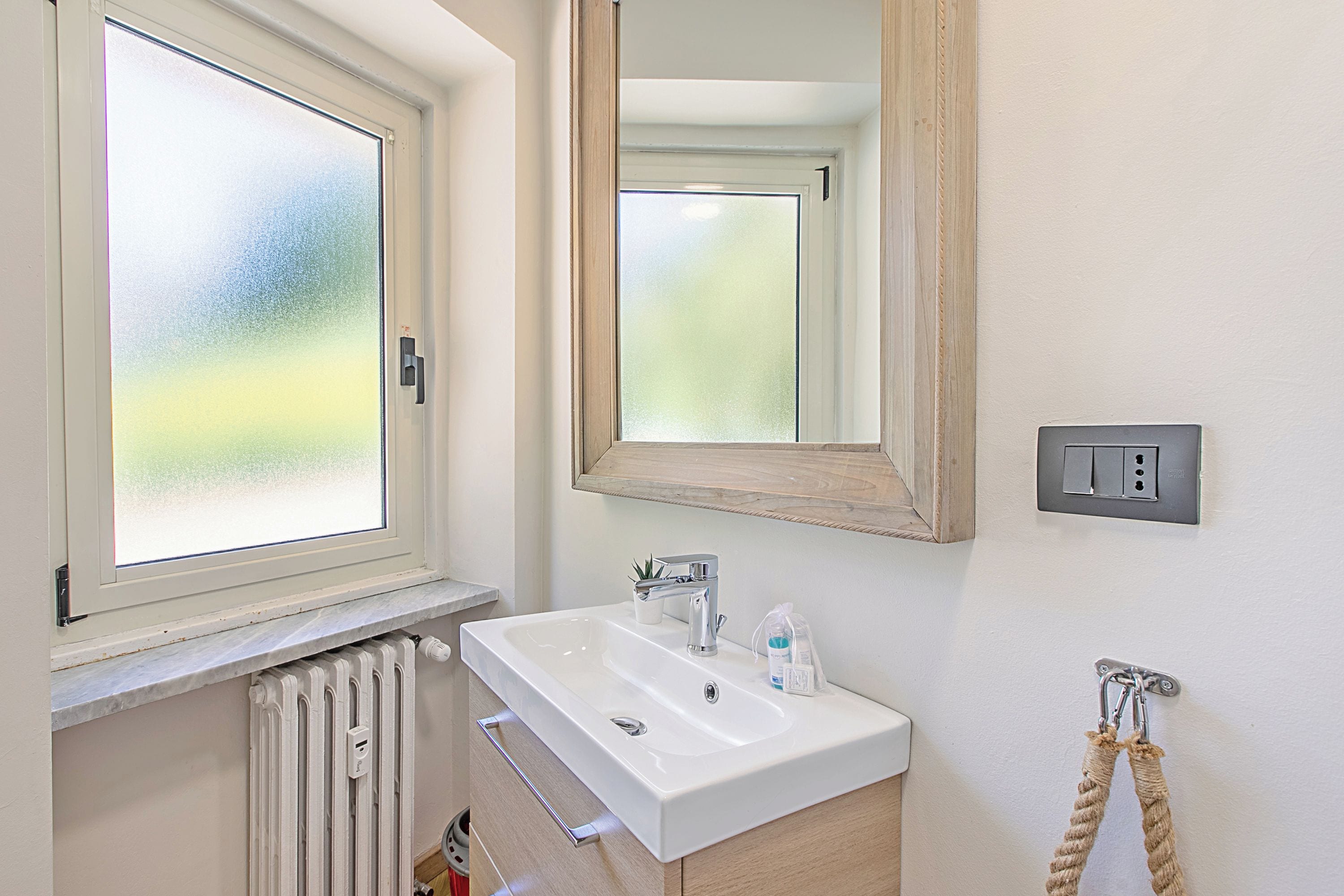 A bathroom with a window, a sink, a mirror, a towel rack, and a radiator.