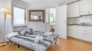 Un dormitorio con cama, lámpara de noche, espejo y vistas a una cocina con armarios y estufa.
