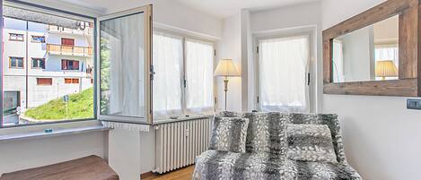 A room with a sofa, a lamp, and a view of a building with balconies.