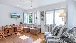 Una sala de estar bien iluminada con un sofá, una mesa de comedor con sillas, un televisor y una ventana con cortinas.