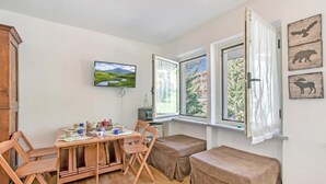 Una habitación con una mesa de comedor, sillas, un televisor y una ventana con cortinas.