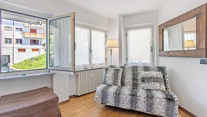 A room with a sofa, a lamp, and a view of a building with balconies. - Gran Roc 9 (Sestriere)