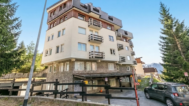 Un edificio de varios pisos con balcones, una entrada cubierta y vistas a la montaña.