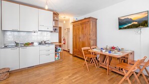 A compact kitchen with white cabinets, a dining area with a wooden table and chairs, and a large wooden wardrobe. - Gran Roc 9 (Sestriere)