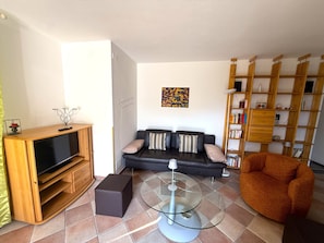 A living room with a flat-screen TV, a glass coffee table, a sofa with striped cushions, a red armchair, and a wooden bookshelf. - Arias Giovanna Visa Lago Villa (Tremosine)
