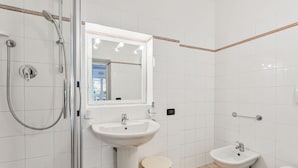 Et badeværelse med en glasvæg omkring brusenichen, et konsolbord med vask, et spejl på væggen og et toilet.