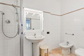 Ein Badezimmer mit Duschkabine, Standwaschbecken, Spiegel an der Wand und Toilette.