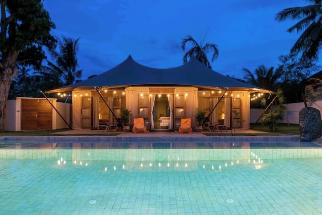 A poolside area with a covered seating area, a pool, and palm trees in the background.