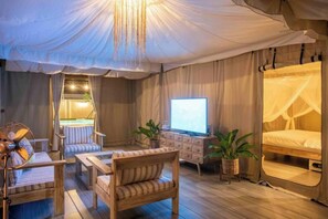 A tented room with a bed, a television, a fan, and a seating area with a table and chairs. - 2 bedrooms luxury glamping tent (Koh Samui)