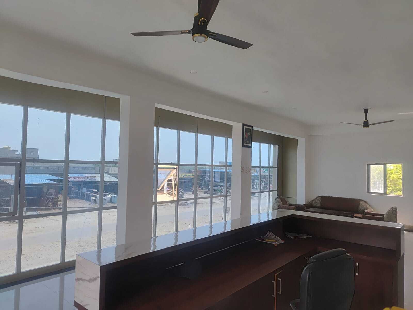 Una habitación con amplias ventanas, un escritorio, una silla y ventiladores de techo.