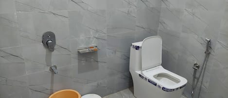 A bathroom with a toilet, bidet, and shower. There are two buckets and a small stool.