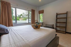 A bedroom with a large bed, a window with curtains, a bedside table, and a wooden shelf. - 2 bedrooms pool villa in peaceful garden (Koh Samui)