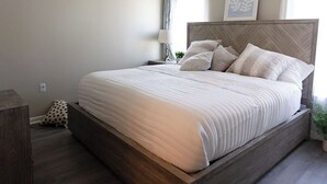 Een slaapkamer met een bed, een plafondventilator, een nachtkastje, een lamp en een raam met gordijnen.