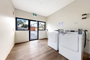 A laundry room with two front-loading washing machines, a dryer, and a window providing a view of the outside. - Private Ensuite Room | Near UniMelb & CBD | Sleeps 3 (Carlton)