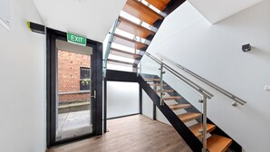 Ein modernes Interieur mit einer Holztreppe, einer Glastür zum Außenbereich und einem sichtbaren Fluchtweg.