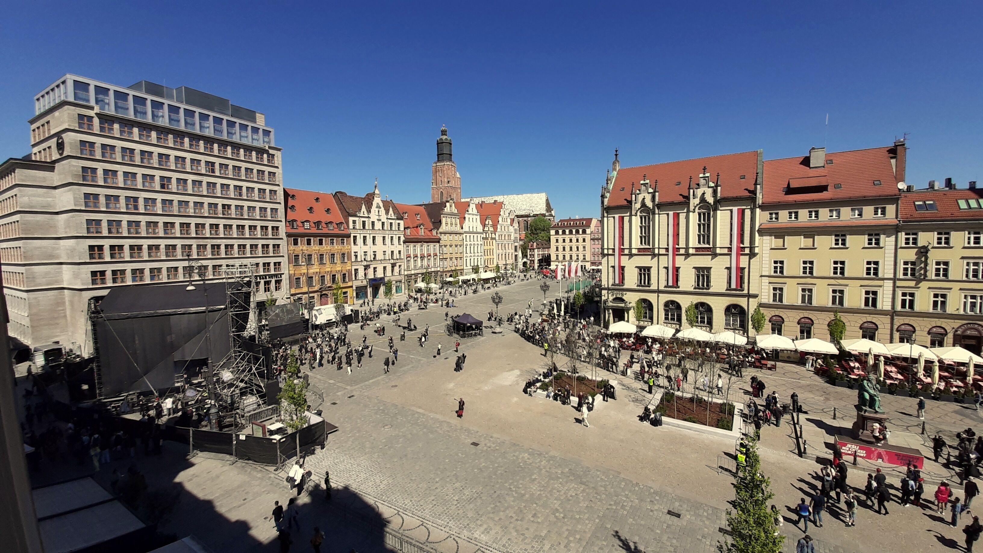 A public square with historic buildings, a prominent tower, and outdoor seating areas.
