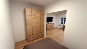 A room with a large wardrobe, a television on a stand, and a window with a view. - New, exclusive apartment on Breslauer Ring with a breathtaking view of City Hall! (Breslau)