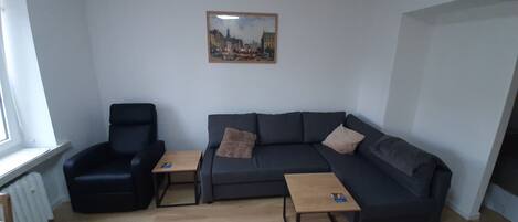 A living room with a black armchair, a dark grey sofa, and two small wooden tables.