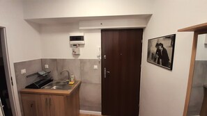 A compact kitchen with a sink, a wooden cabinet, a dark door, and a wall-mounted light fixture. - New, exclusive apartment on Breslauer Ring with a breathtaking view of City Hall! (Breslau)