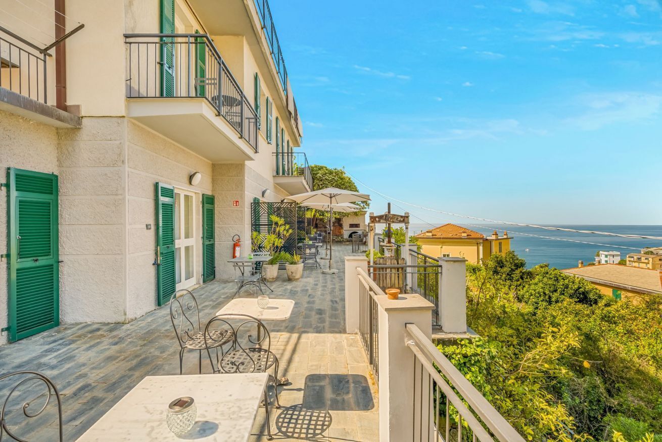 Un balcon avec des sièges d’extérieur, une vue sur la mer et un bâtiment aux volets verts.