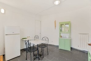 Eine kleine Küche mit einem weißen Kühlschrank, einem Esstisch mit vier Stühlen und einem grünen Schrank.