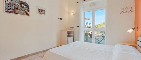 A bedroom with a bed, a small cabinet, a window with a view, and wall-mounted artwork.