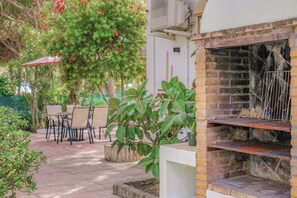 En udendørs terrasse med en murstensgrill, et bord med stole og plantekrukker.