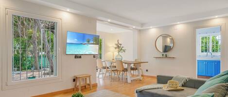 Een moderne woonkamer met een flatscreentelevisie, een eethoek en een keuken met blauwe kastjes.