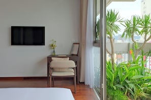 A hotel room with a bed, a desk with a chair, a television mounted on the wall, and a view of greenery and buildings through the window. - Marisol Hotel (Da Nang)