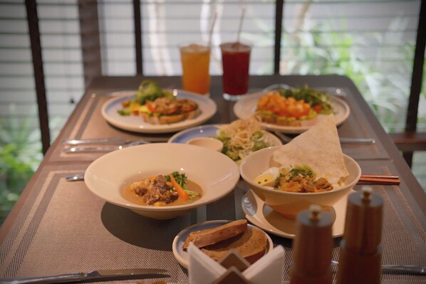 Mesa posta com diversos pratos, incluindo sopa, salada e pão, além de uma bebida e acompanhamentos ao fundo.
