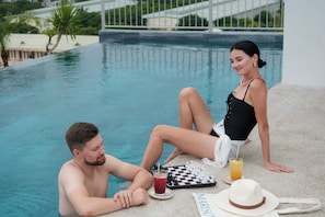 A poolside setting with a chessboard, a drink, and a hat. - Marisol Hotel (Da Nang)